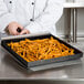 A chef using a TurboChef aluminum paddle peel to remove a tray of french fries from an oven.