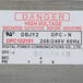 A white sticker with red text reading "Danger High Voltage" on a power supply.