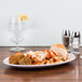 An oval white melamine plate with black trim holding pasta and meatballs on a table.