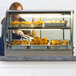 A woman using tongs to put food in a Vollrath countertop display case.