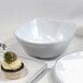 A white curved square bowl with black trim on a white background with a cupcake on it.