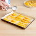 A person pouring sugar into a tray of peaches in a rectangular tart pan.