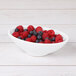 A white Elite Global Solutions melamine bowl filled with raspberries and blueberries.
