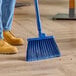 A person sweeping the floor with a blue Carlisle broom.