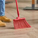 A person sweeping the floor with a red Carlisle angled broom head.