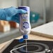 A person in blue gloves using Bar Keepers Friend Liquid Cooktop Cleaner to clean a stove.