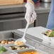 A person in gloves holding a white Elite Global Solutions spoon over food.