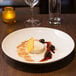 A white porcelain soup bowl with dessert and fruit on it, including a slice of orange.