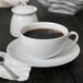 A white porcelain cup of coffee and saucer on a table with a spoon.