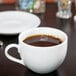 A white cup of coffee with a white saucer on a table.