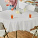 A woman pouring liquid onto a table with a white Creative Converting tablecloth and glasses of liquid.