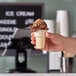 A hand holding a JOY gluten-free cake cone filled with chocolate ice cream.