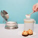 A hand using a wooden spoon to pour sugar into a cup of coffee on a white background.