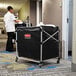 A man in a white shirt pushing a Rubbermaid X-Cart with a black bag.