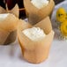 A Hoffmaster unbleached natural tulip baking cup with a cupcake decorated with white frosting and a yellow flower.