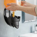 A person using a Kutol hand soap dispenser to pour orange liquid into it.