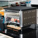 A Nemco conveyor toaster on a counter with two slices of bread in it.