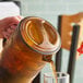 A person pouring a drink from a GET amber pitcher into a glass on a table.