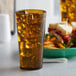 An amber plastic tumbler of ice tea next to a plate of food.