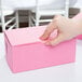 A hand holding a pink cake box with a pink handle.