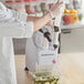 A person in white gloves using an AvaMix Continuous Feed Food Processor to slice cucumbers.