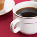 A CAC bright white porcelain coffee cup filled with coffee sits on a table next to a muffin.