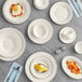 Acopa ivory wide rim stoneware plates on a table with bowls and silverware.