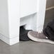 A person's foot stepping on a white rectangular Rubbermaid step-on container.