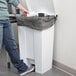 A man using a Rubbermaid white rectangular step-on trash can with a black plastic bag inside.