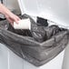 A hand holding a white cup in a Rubbermaid white rectangular step-on trash can.