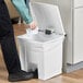 A person using a Rubbermaid white rectangular step-on trash can to throw away paper.