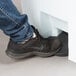 A person's foot stepping on a white Rubbermaid step-on trash can pedal.