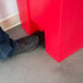 A person's foot stepping into a Rubbermaid red rectangular step-on trash can.