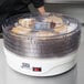 A Weston 4-tier food dehydrator on a counter with clear containers of food inside.