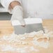 A person using a Tablecraft stainless steel dough cutter with a white handle to cut dough.