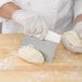 A person using a Tablecraft stainless steel dough cutter with a white handle to cut dough.