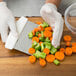 A person using a Tablecraft stainless steel bench scraper to cut carrots on a cutting board.