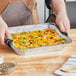 A hand using a Western Plastics foil steam table pan to serve a meal.