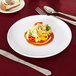 A Carlisle white melamine plate with food and a knife on it.
