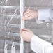 A person in a white lab coat unzipping a clear plastic bun pan rack cover.