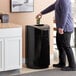 A man opening a Rubbermaid Eclipse black round waste receptacle with a rigid plastic liner.