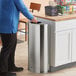 A man standing next to a Rubbermaid stainless steel half round trash can.