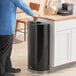 A man throwing a paper cup into a Rubbermaid half round open top trash can.