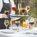 A waiter holding a tray of Acopa Balloon Wine Glasses filled with red and orange wine.