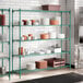 A large green wire shelving unit with multiple shelves holding various kitchen dishes and containers.
