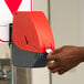 A person's hand using a red Turn-O-Matic ticket dispenser.