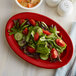 A white Tuxton oval china platter with salad, tomatoes, cucumbers, and lettuce on it.