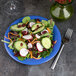 A vegetable salad with cucumbers, radishes, and carrots on a Carlisle Ocean Blue melamine plate.