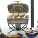 A buffet table with a black Vollrath wire chafer stand holding a large chafing dish of food and fruit.