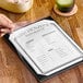 A hand holding a clear vinyl sheet protector with a menu inside.